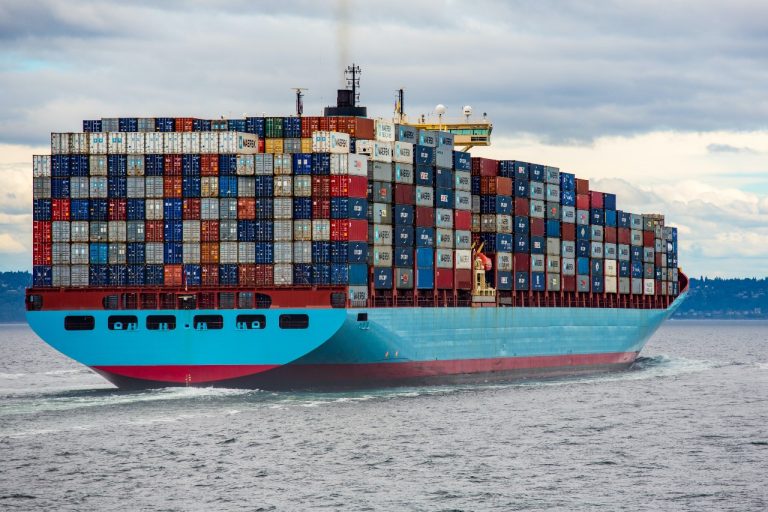 Sky blue cargo ship underway with shipping containers stacked high on deck
