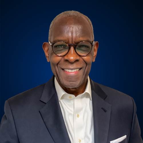 Professional headshot of Jim Roberts wearing glasses, a navy blazer, and a white dress shirt, smiling against a dark blue background.