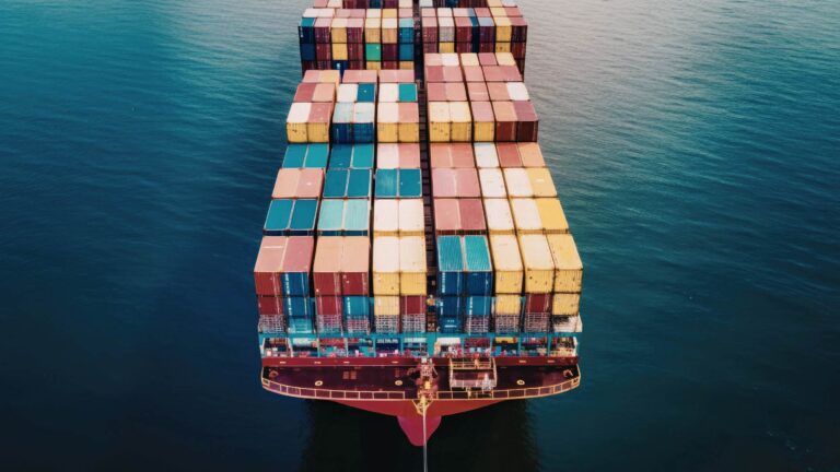 Aerial view of a container ship at sea carrying multicolored shipping containers, symbolizing global ocean freight and trans-Pacific trade.