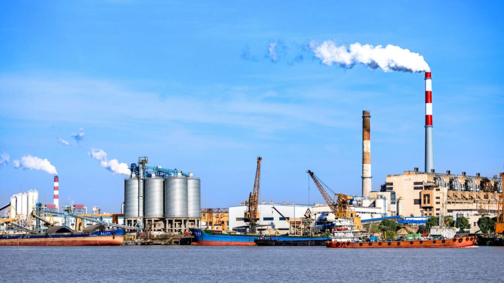 Industrial manufacturing plant and cargo ships at a port illustrating global manufacturing overcapacity and international trade.