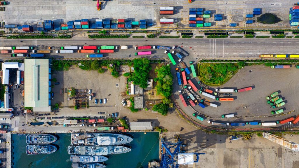 Aerial view of cargo containers, freight trucks, rail transport, and shipping vessels at an international port illustrating global trade logistics, supply chain operations, customs compliance, and duty drawback services.
